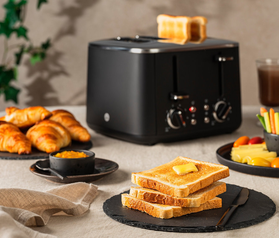 Auf einem Tisch steht ein schwarzer WILFA Toaster FAMILY, daneben Croissants, Toast mit Butter und Gemüse.