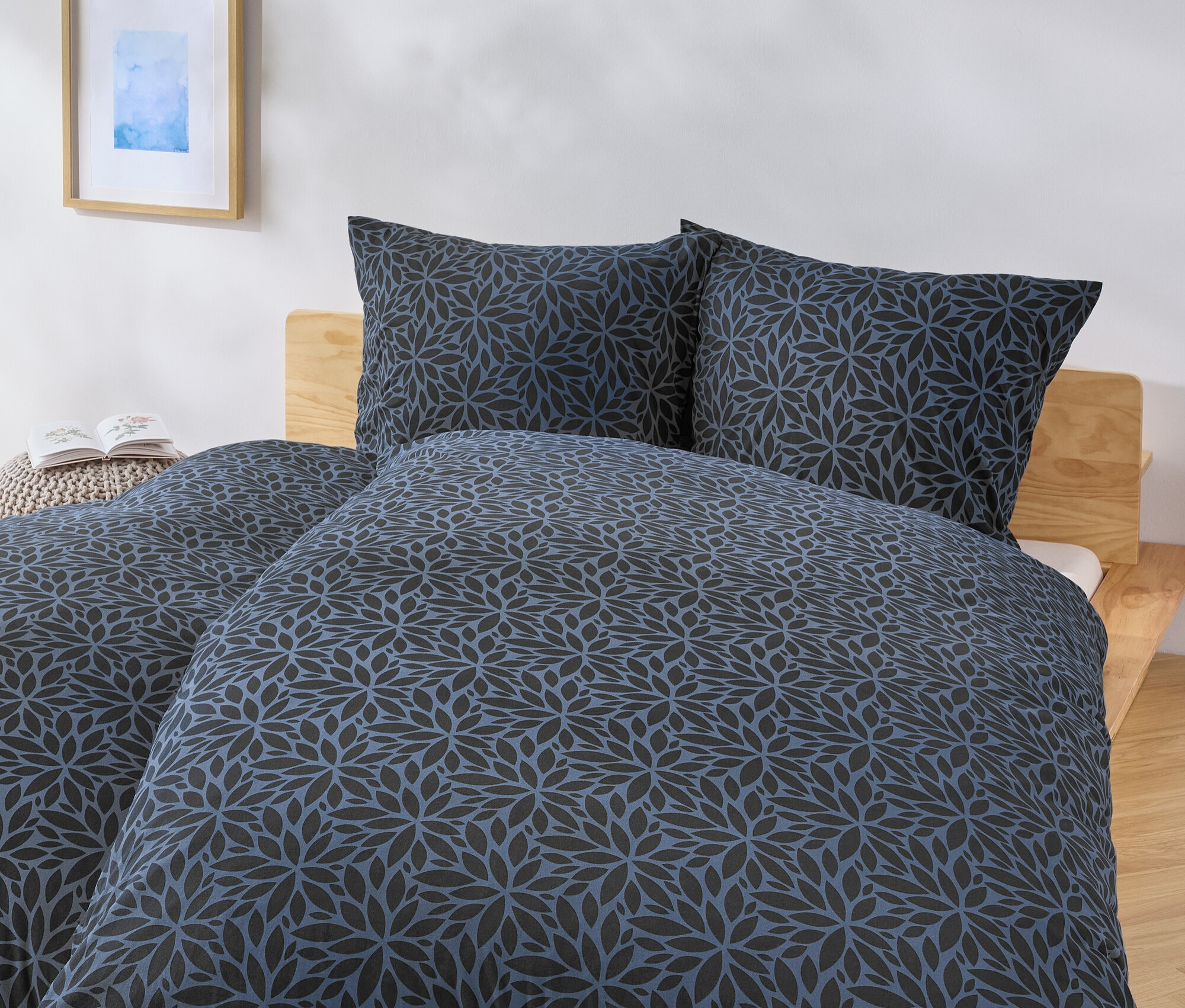 Bett mit blau-schwarzer Blumendecke und zwei Kissen.