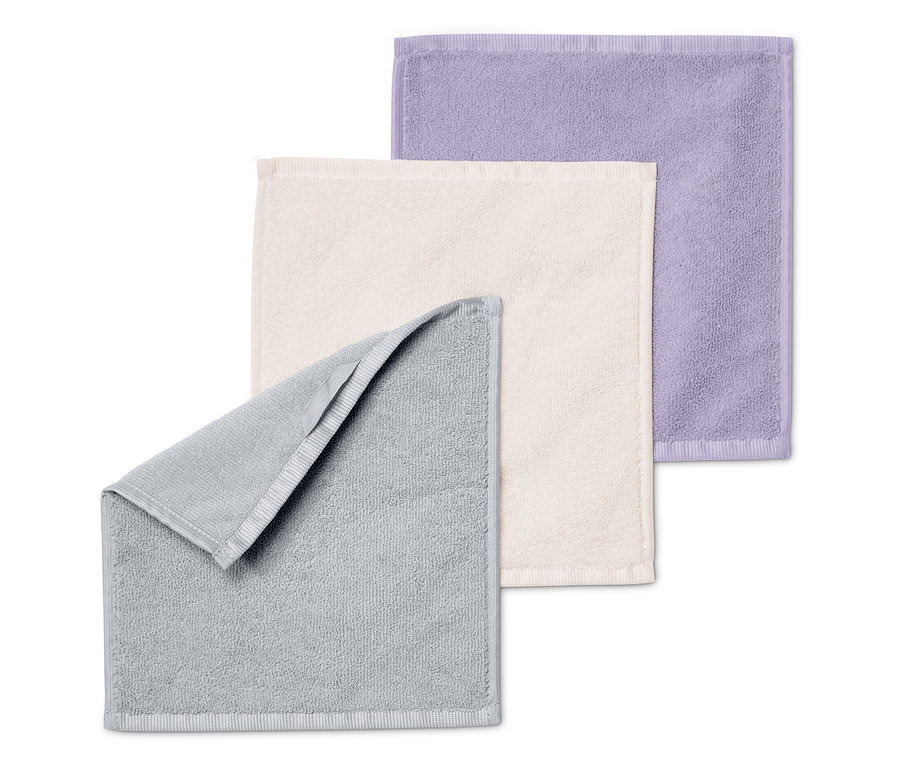 Drei Handtücher liegen übereinander: grau, creme und lila.