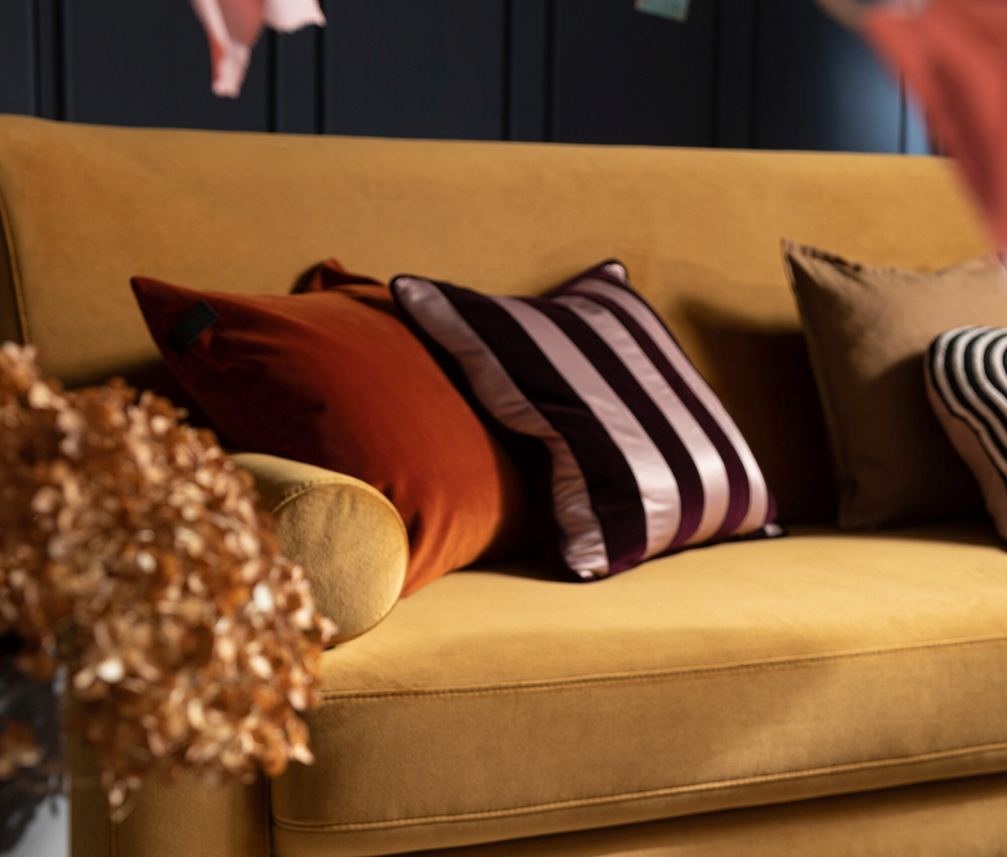 Gelbes Sofa mit orangefarbenen und gestreiften Kissen.