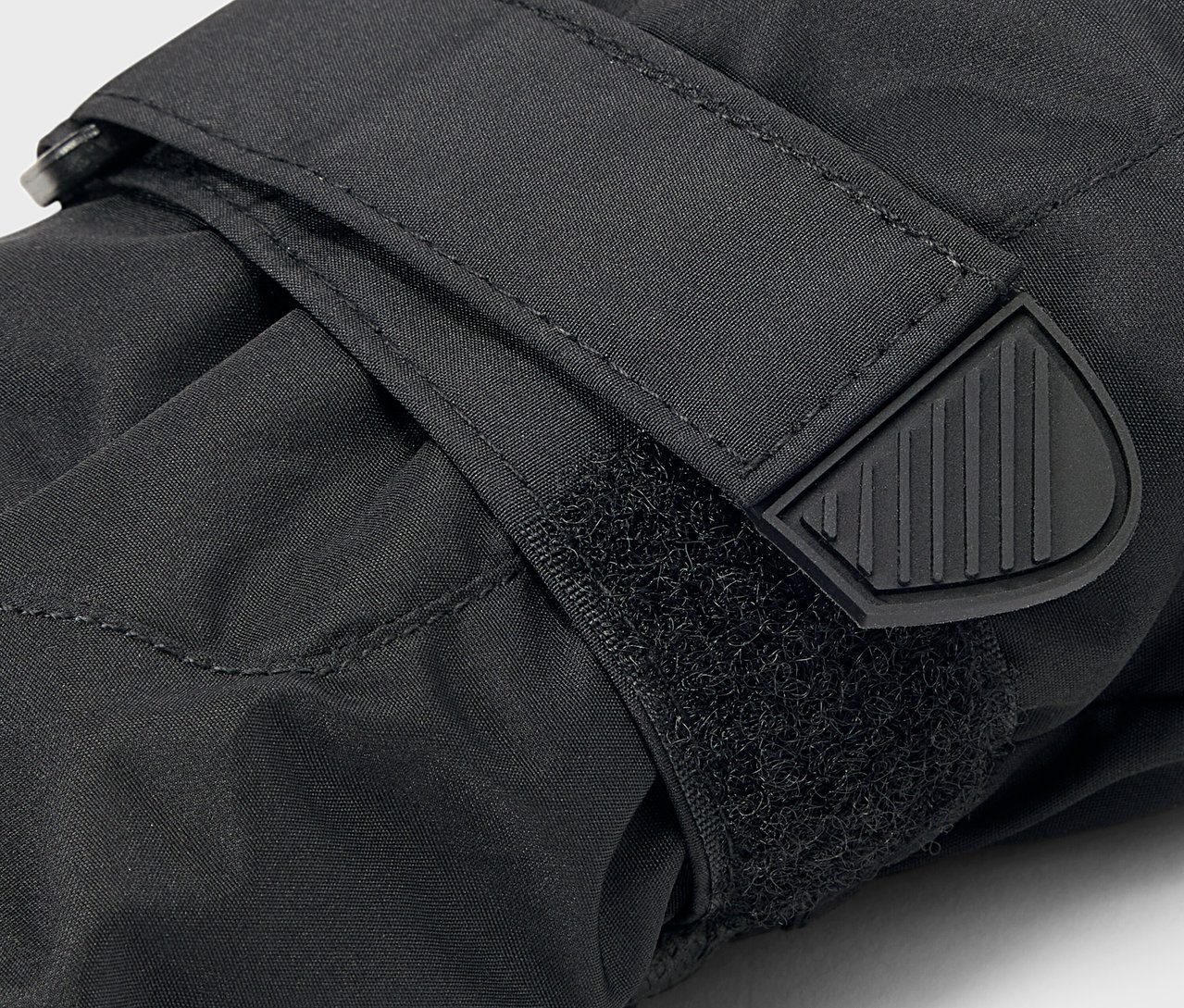 Detailaufnahme eines schwarzen Handschuhs mit Klettverschluss und Gummiabschluss am Riemen.