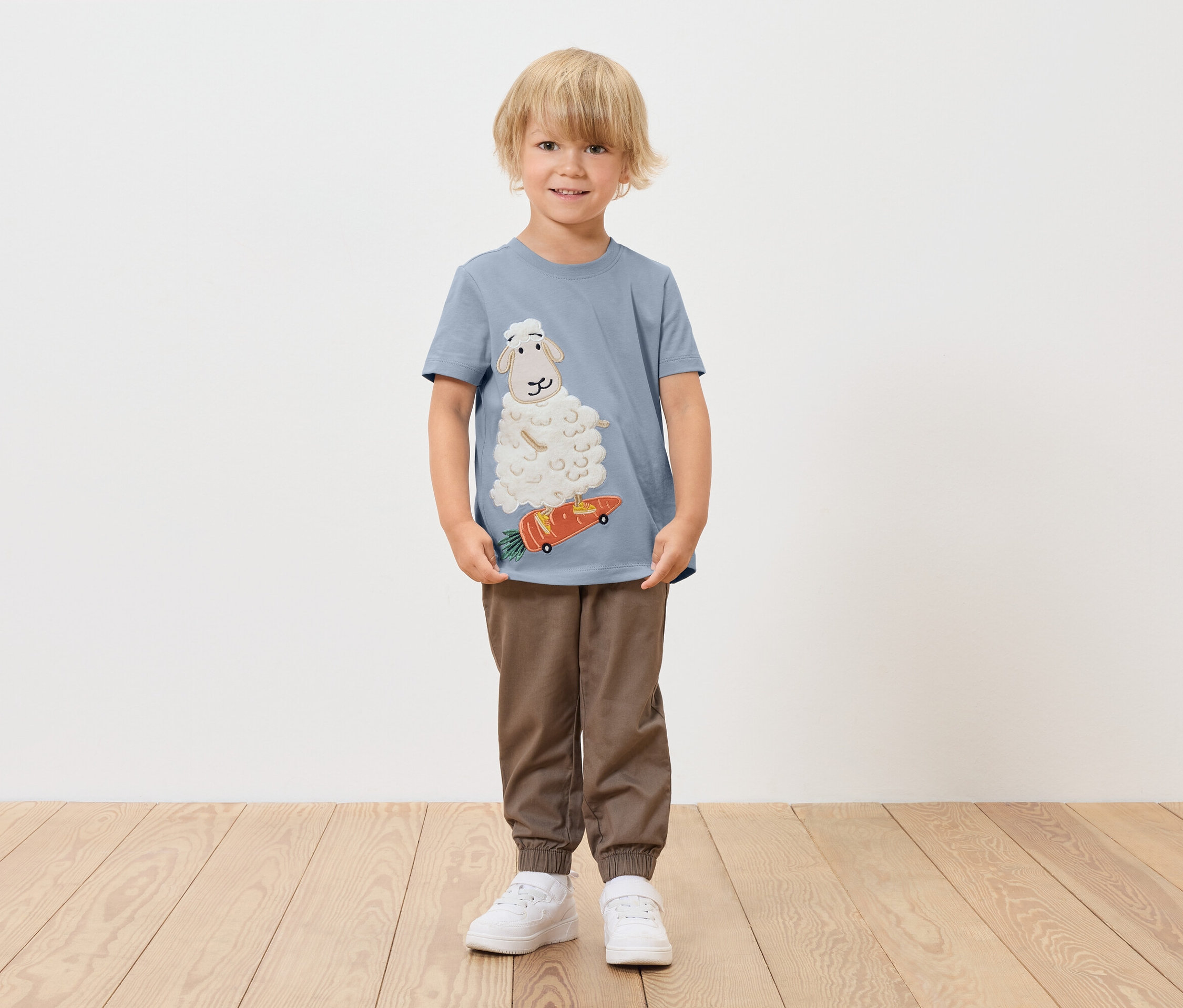 Junge trägt ein blaues T-Shirt mit einem Schaf auf einem Karotten-Skateboard.