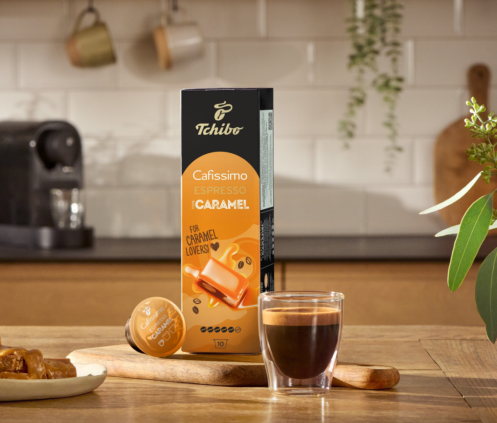Espresso, Karamellbonbons und eine Packung Cafissimo Flavoured Edition – Espresso Caramel - 80 Kapseln auf einem Holztisch.