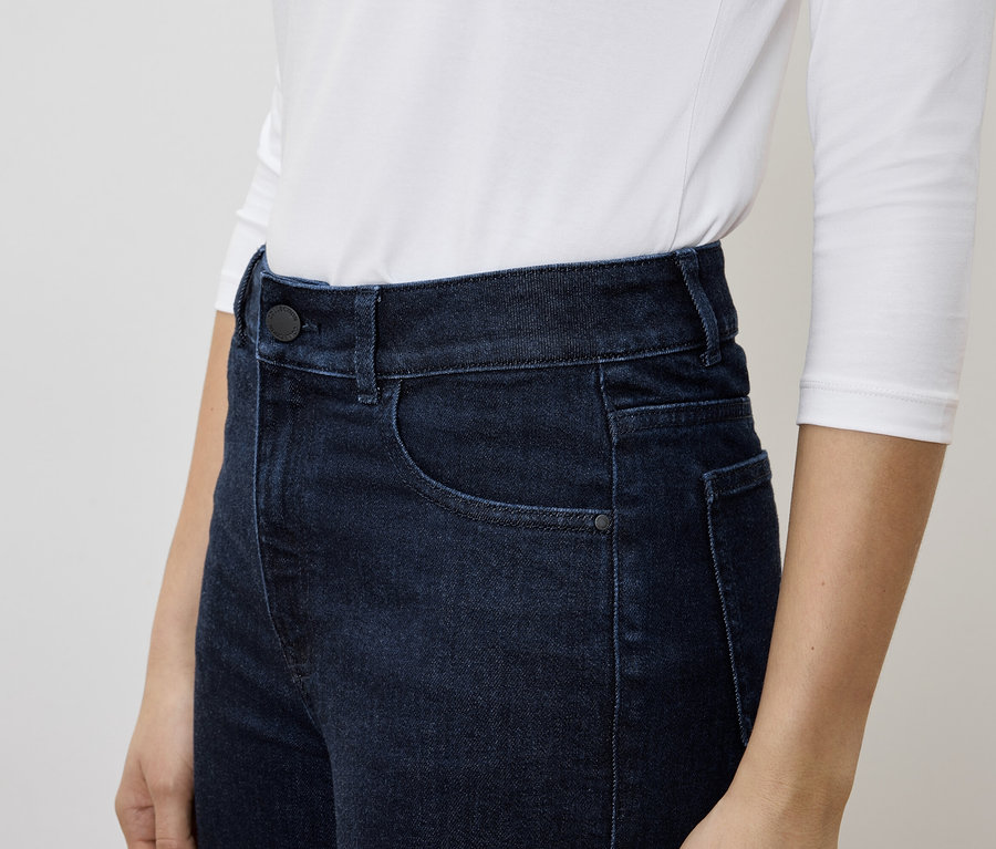 Eine Frau trägt dunkelblaue Jeans und ein weißes Langarmshirt.