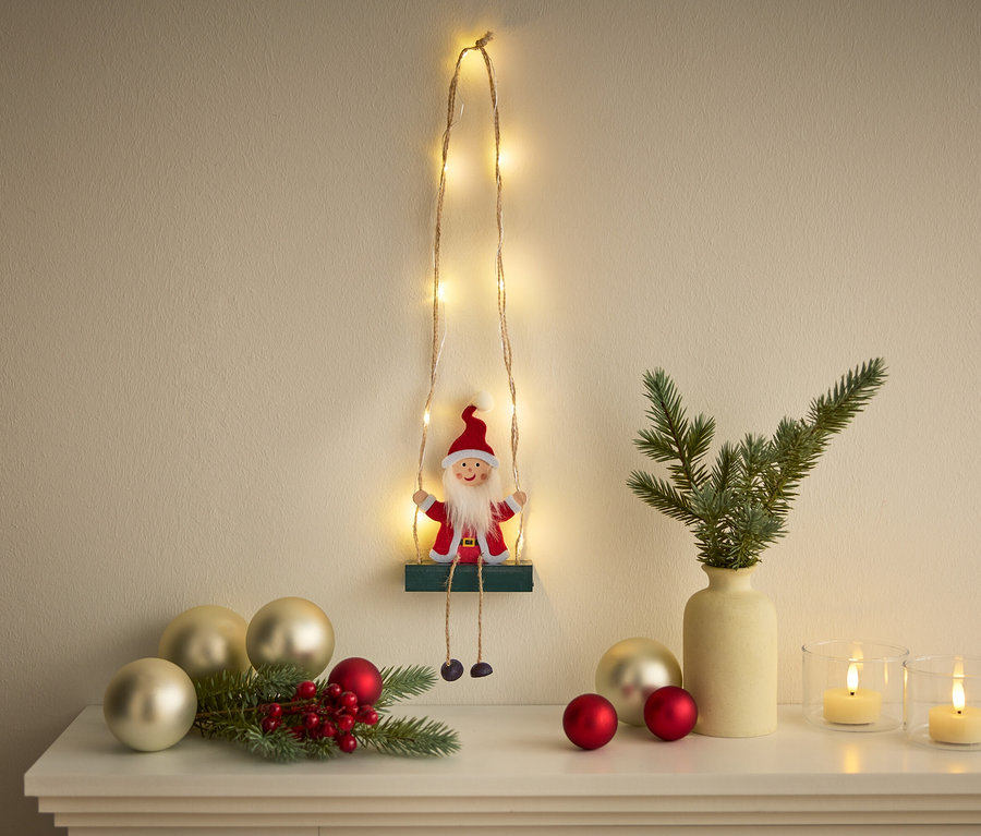 Dekoration mit einem Santa Claus-Motiv auf einer an der Wand hängenden Schaukel, ergänzt durch eine Lichterkette und Weihnachtsschmuck.