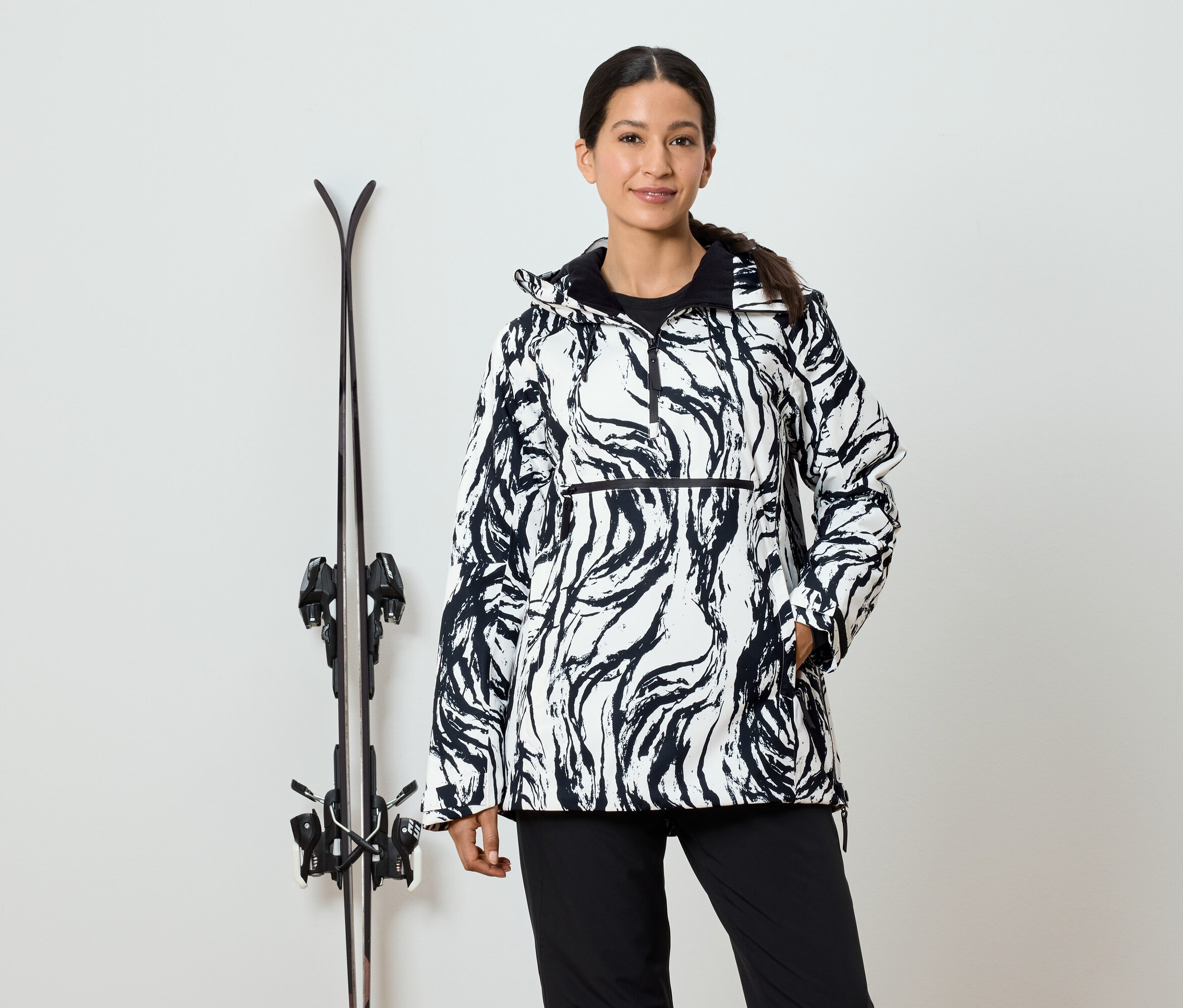 Frau in schwarz-weißer Musterjacke steht neben Skiern.