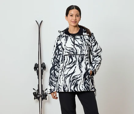 Frau in schwarz-weißer Musterjacke steht neben Skiern.