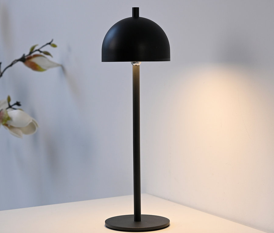 Schwarze Tischleuchte mit rundem Schirm auf einem weißen Tisch.