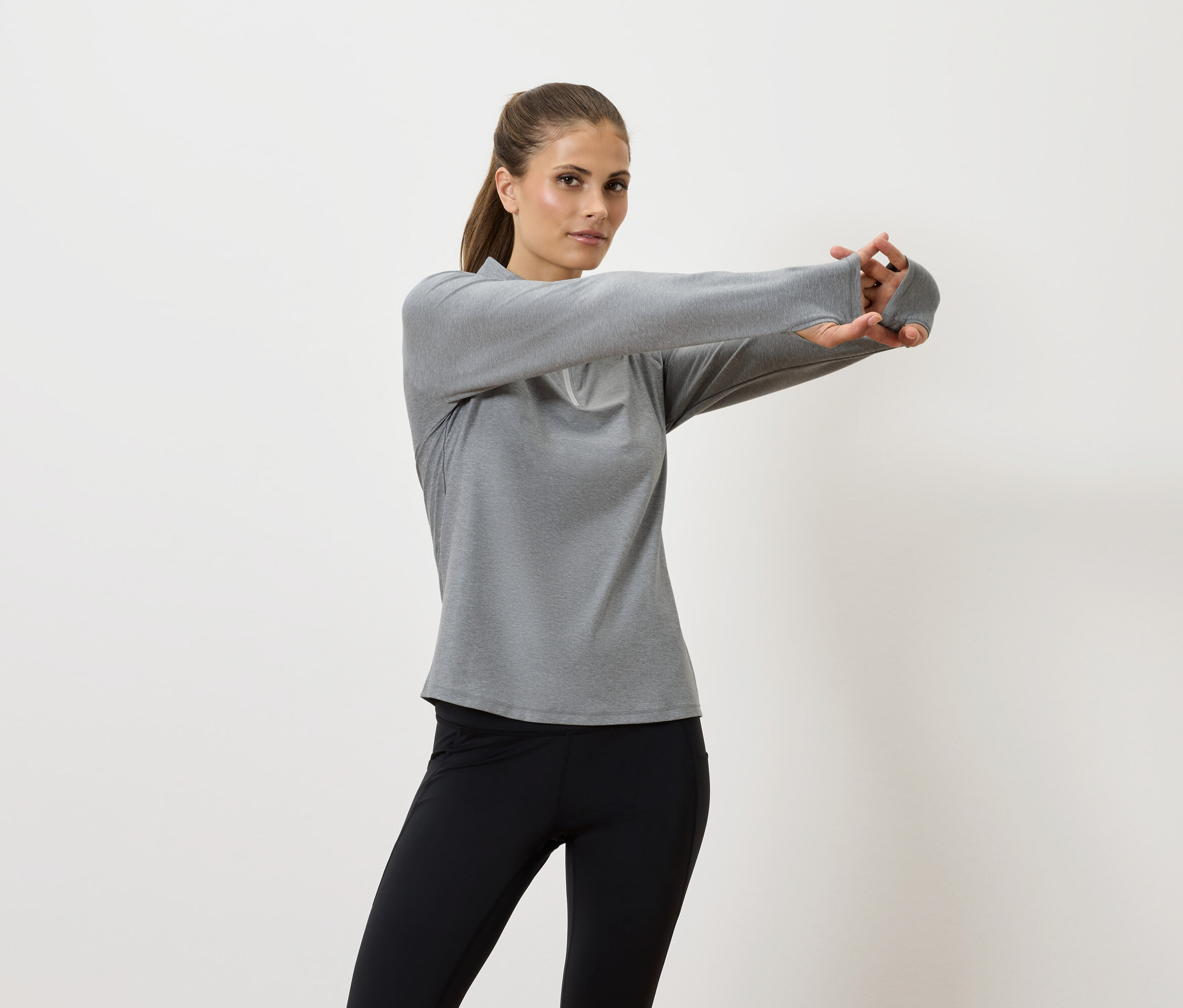 Frau dehnt ihre Arme in einem grauen Langarmshirt und schwarzen Leggings.