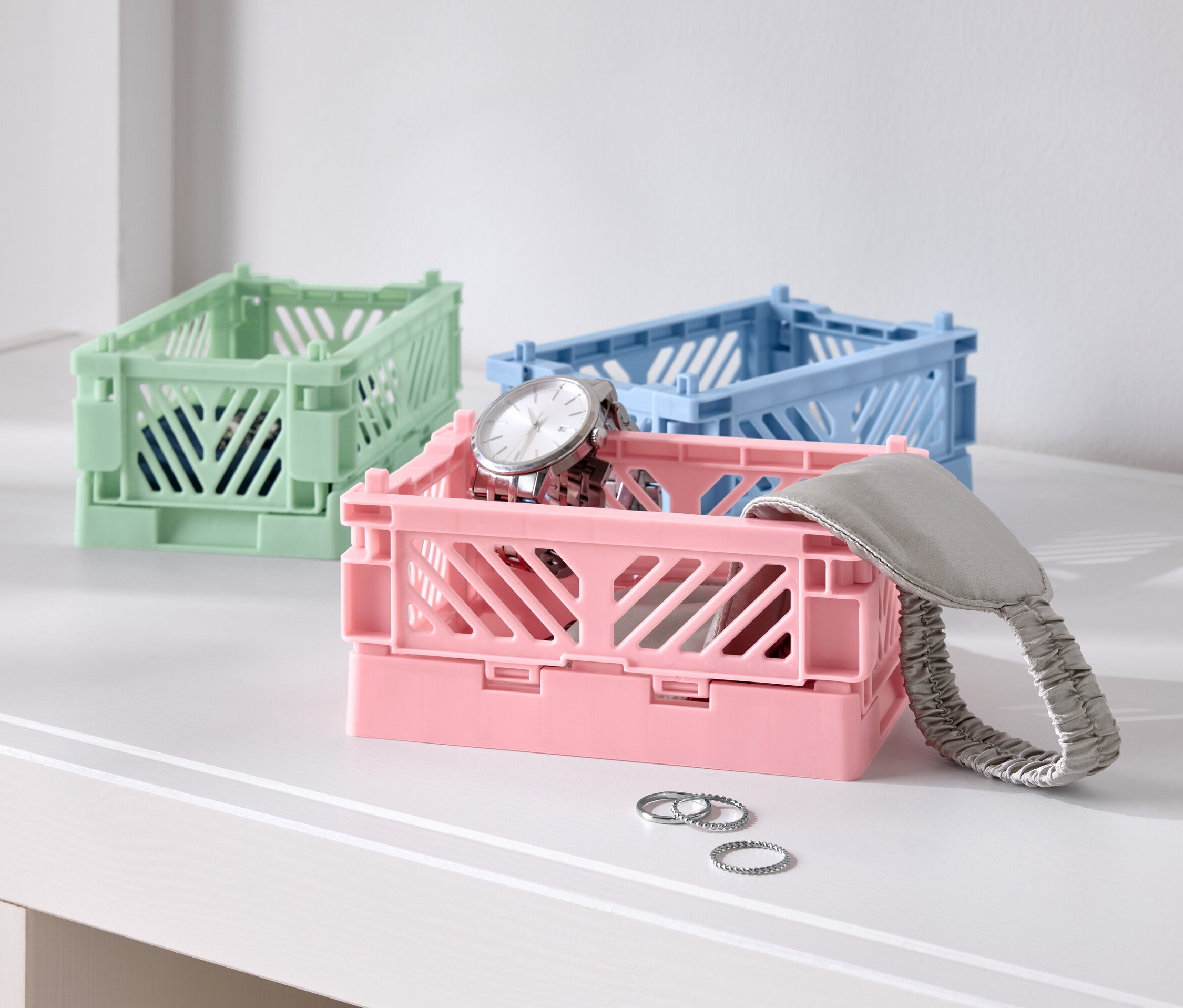 Drei farbige Faltboxen auf einem Tisch, eine rosa mit einer Uhr, eine blaue und eine grüne.