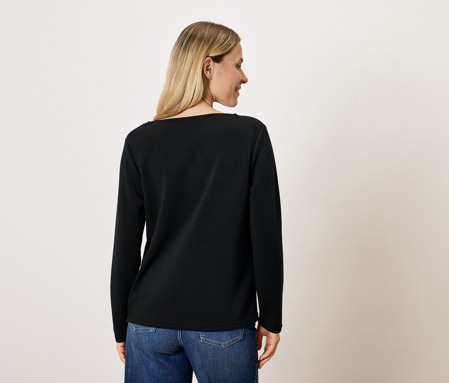 Blonde Frau von hinten in schwarzem Langarmshirt und blauen Jeans.