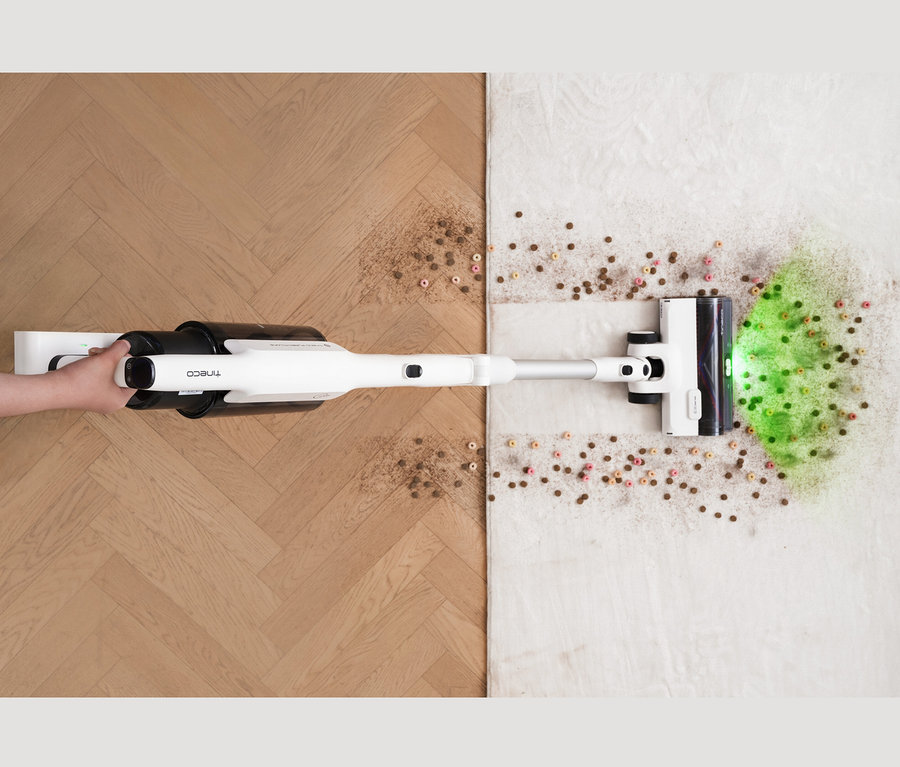 Detailaufnahme einer Person, die einen Tineco Akku-Staubsauger »Pure One A50S« verwendet, um Schmutz von einem Holzboden und einem Teppich zu entfernen.