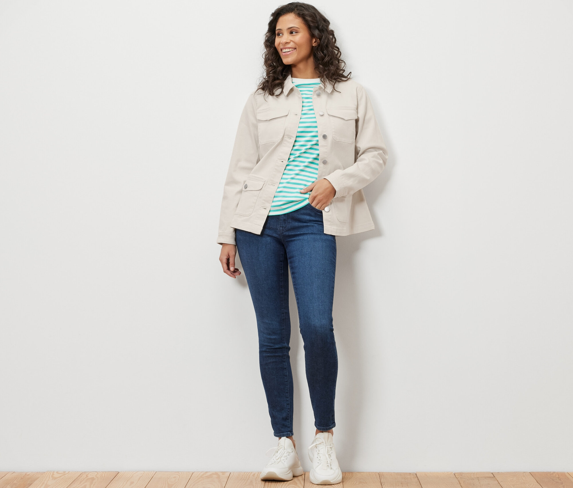 Frau trägt eine Jeansjacke mit Cargo-Taschen, blaue Jeans und weiße Turnschuhe.