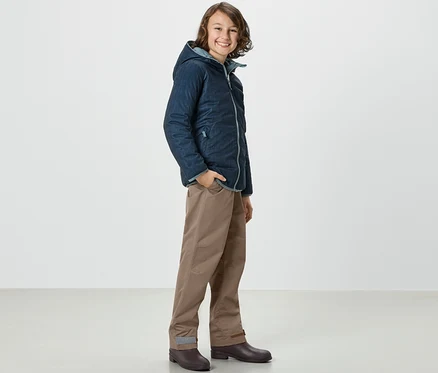 Ein Junge in Jacke und Kinder-Regenhose steht seitlich.