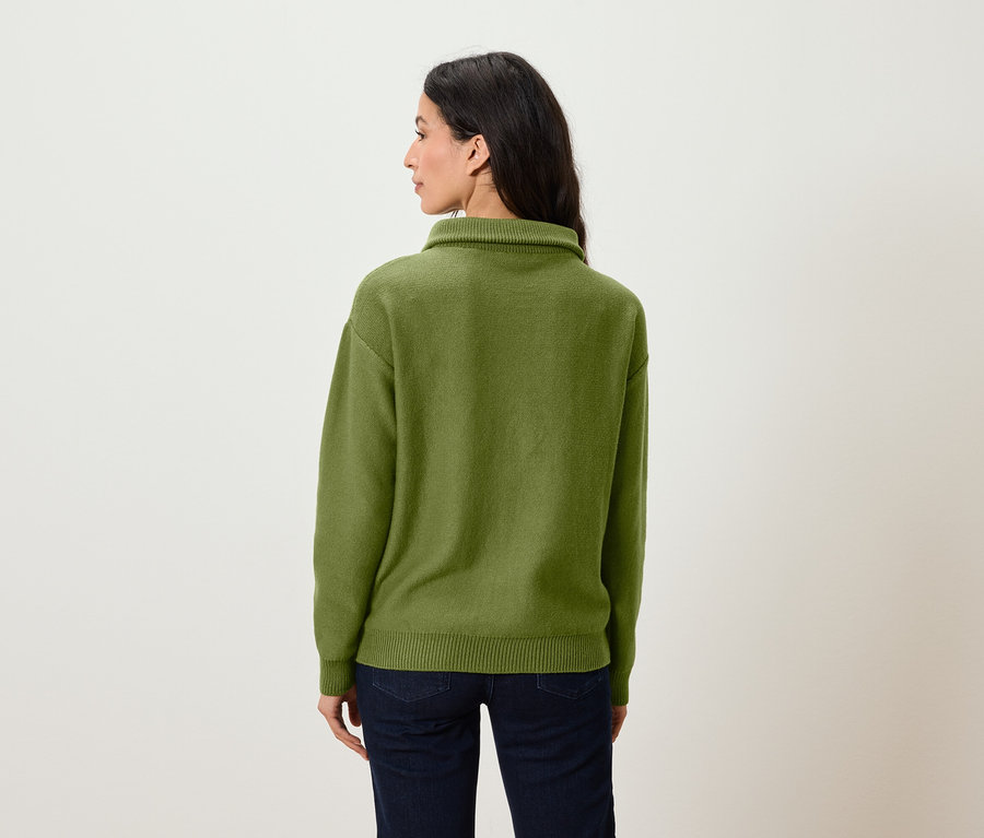 Frau steht mit dem Rücken zur Kamera und trägt einen grünen Pullover und Jeans.