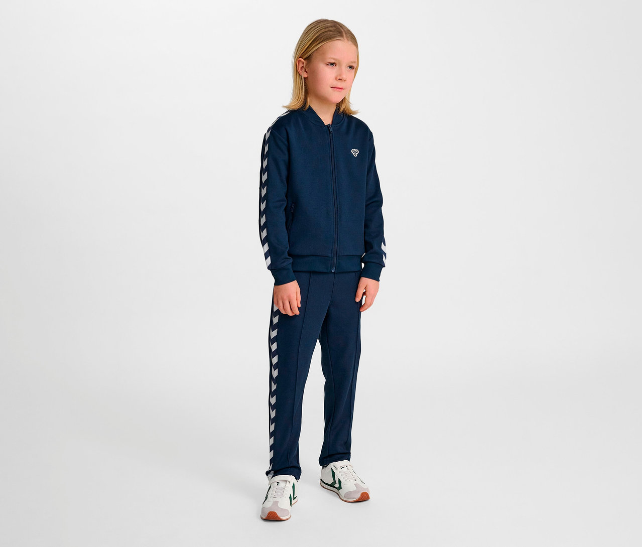 Junge steht im Studiohintergrund im blauen Hummel Trainingsanzug.