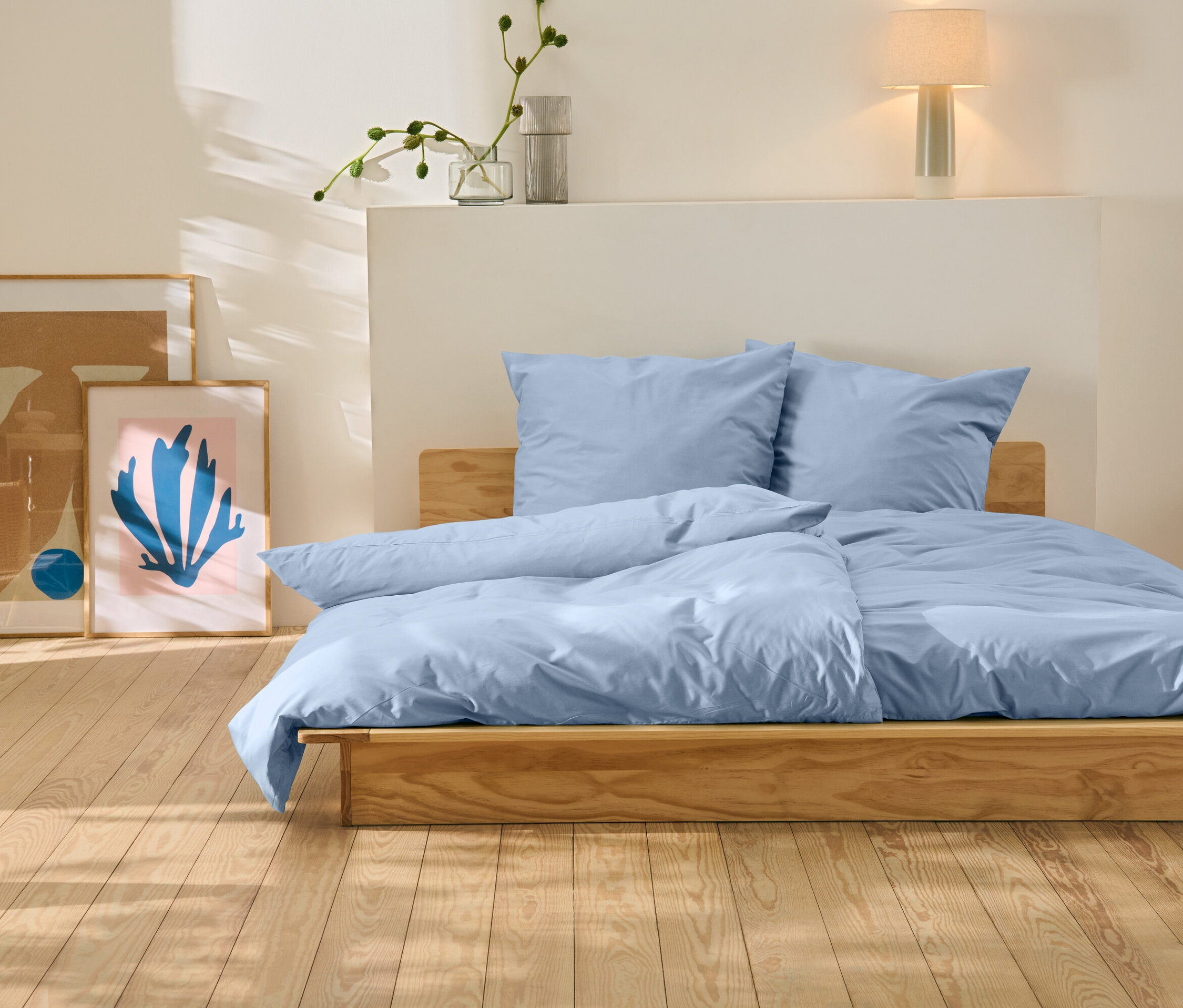 Ein Bett mit blauer Bettwäsche steht auf einem Holzboden. Hinter dem Bett befinden sich zwei Bilder.