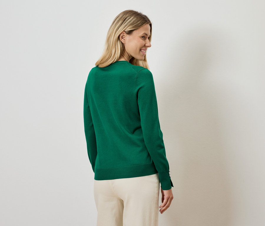 Frau blickt über die Schulter und trägt einen grünen Pullover und eine beige Hose.