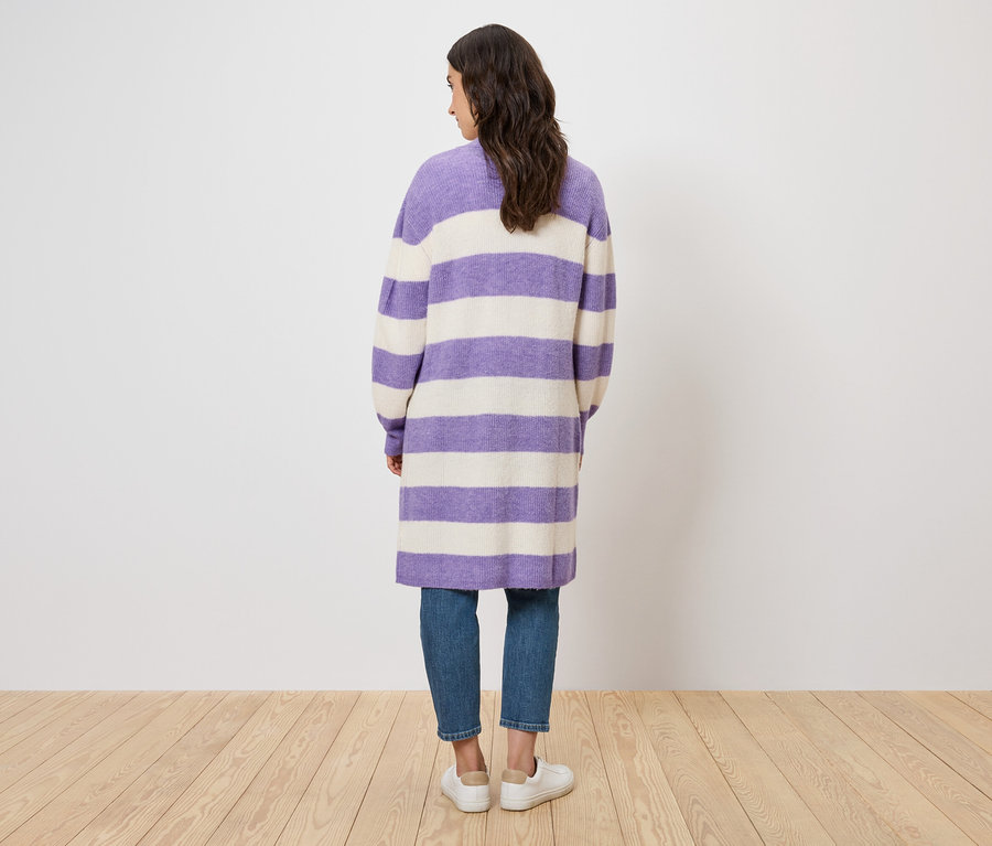 Rückansicht einer Frau, die einen lila-weiß gestreiften Mantel, Jeans und weiße Schuhe trägt.