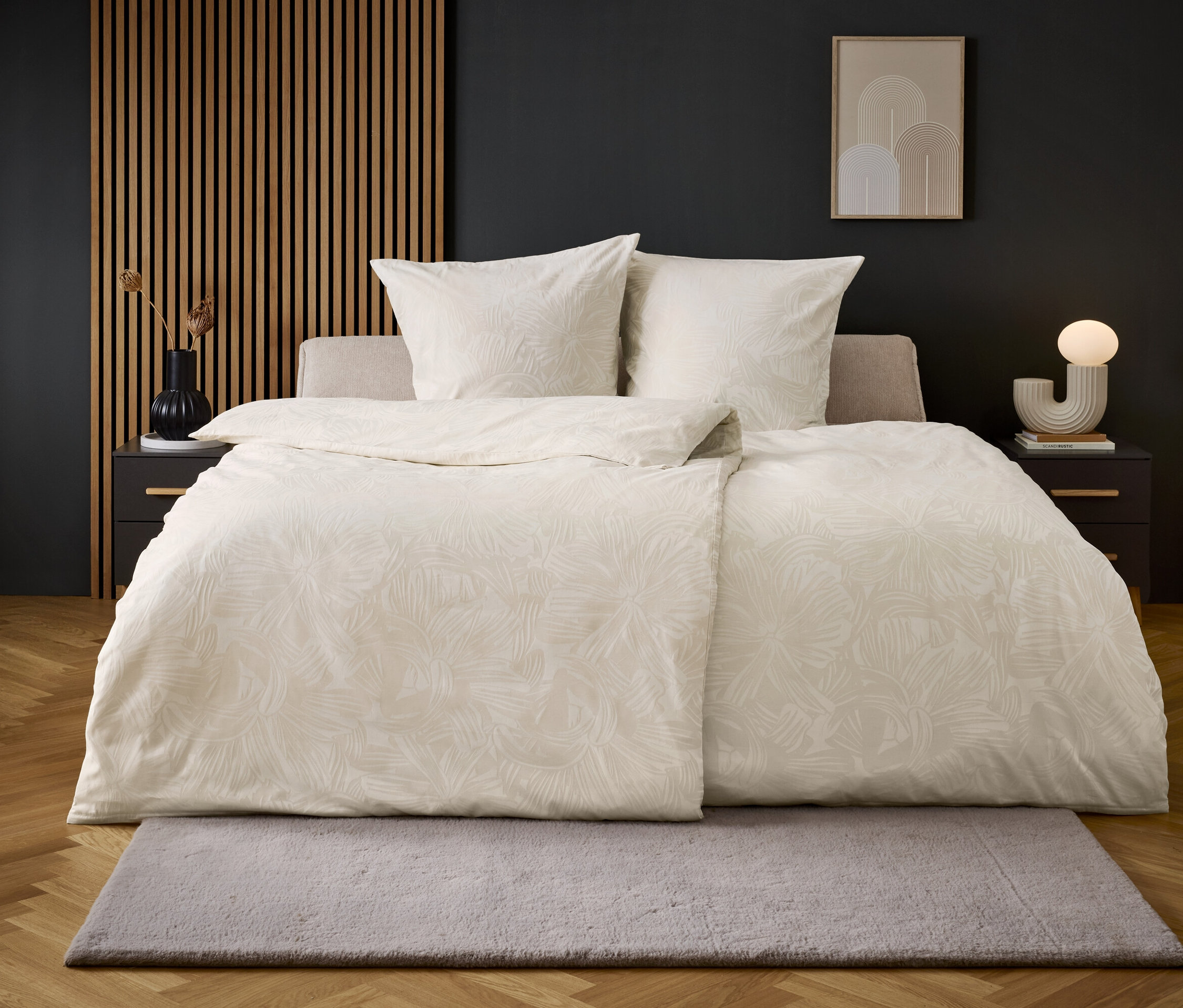 Beiges Bett mit weißer Bettwäsche auf einem Boden mit grauem Teppich.