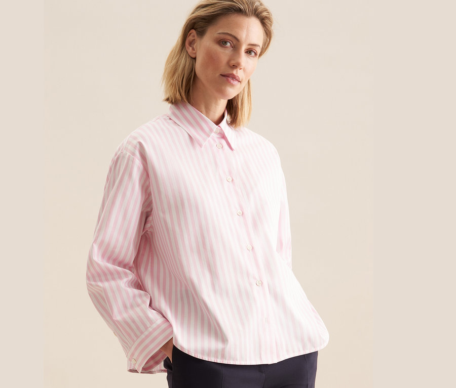Frau trägt eine rosafarbene Seidensticker Oversize Hemdbluse mit Streifen und eine dunkelblaue Hose.