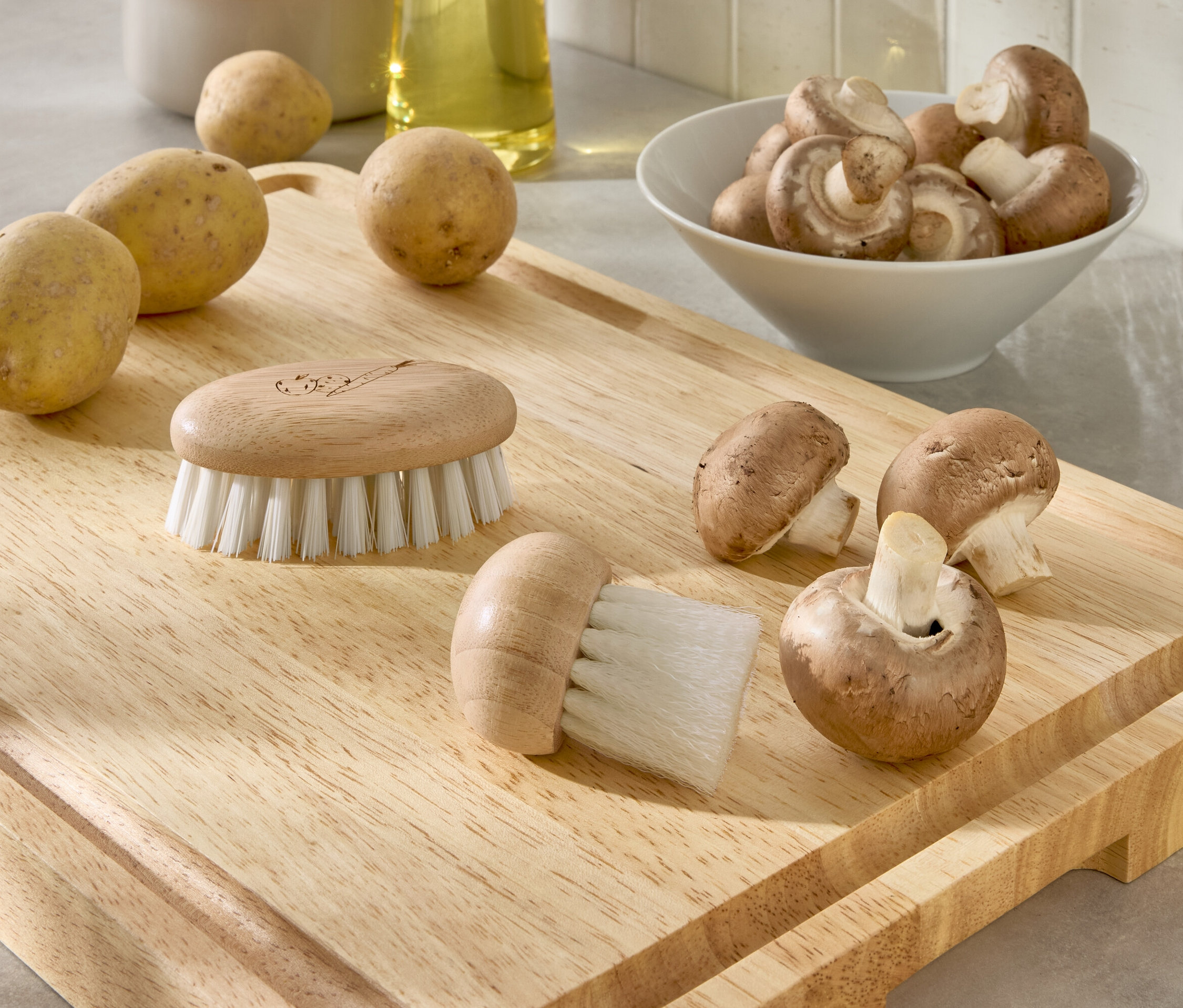 Auf einem Holzbrett liegen Kartoffeln, Pilze und zwei Bürsten.