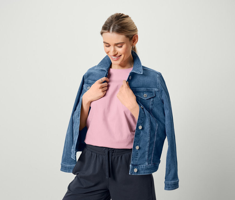 Frau trägt eine Jeansjacke, ein rosafarbenes Basic T-Shirt und Bermuda-Sweatshorts.