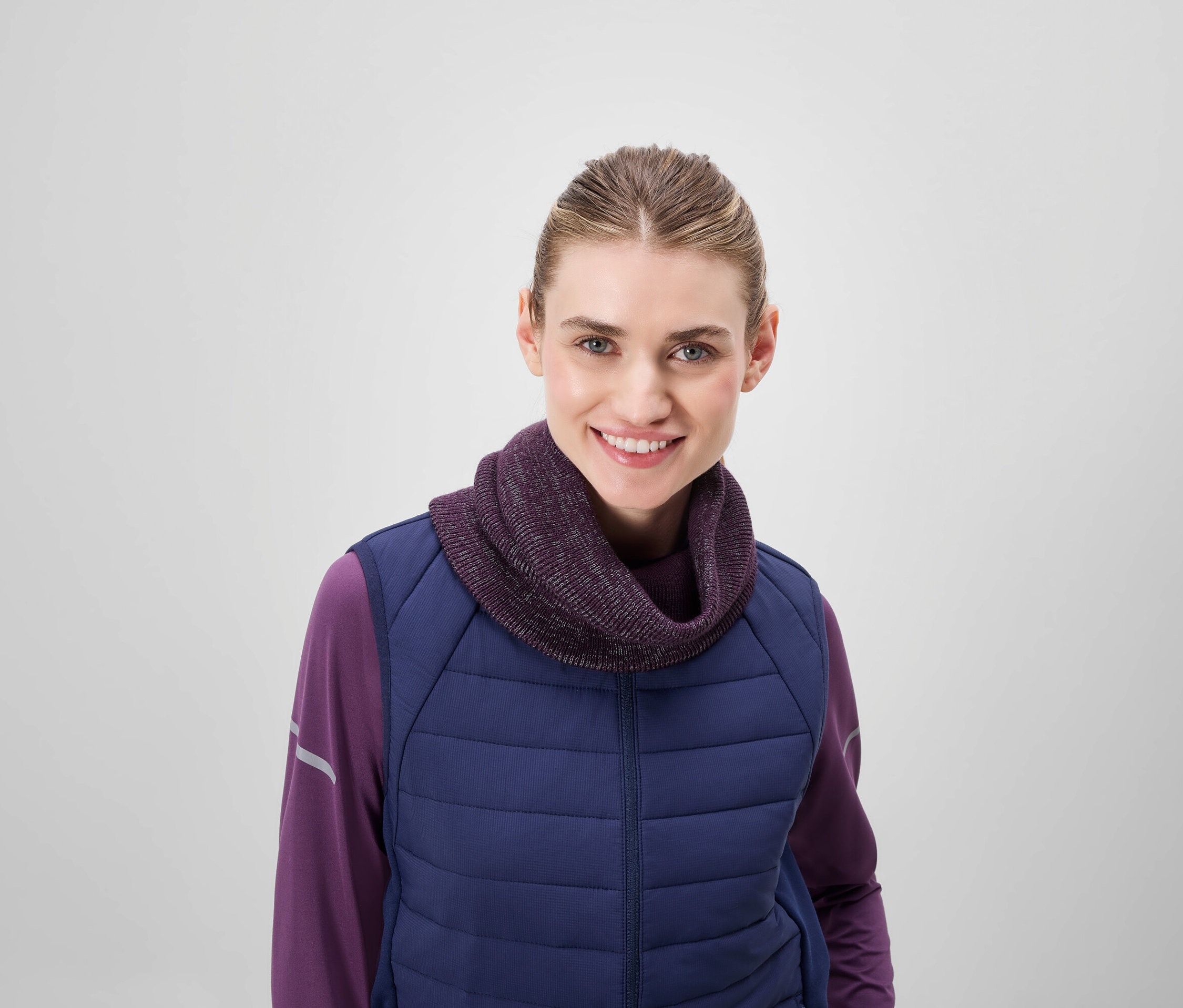 Lächelnde Frau trägt einen lila Rollkragenpullover und eine blaue Steppweste.