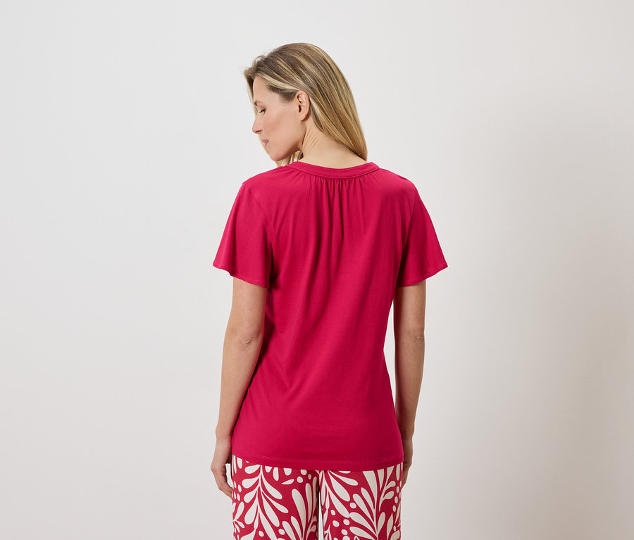 Rückansicht einer Frau mit blonden Haaren, die ein pinkes T-Shirt und rot-weiß gemusterte Hosen trägt.