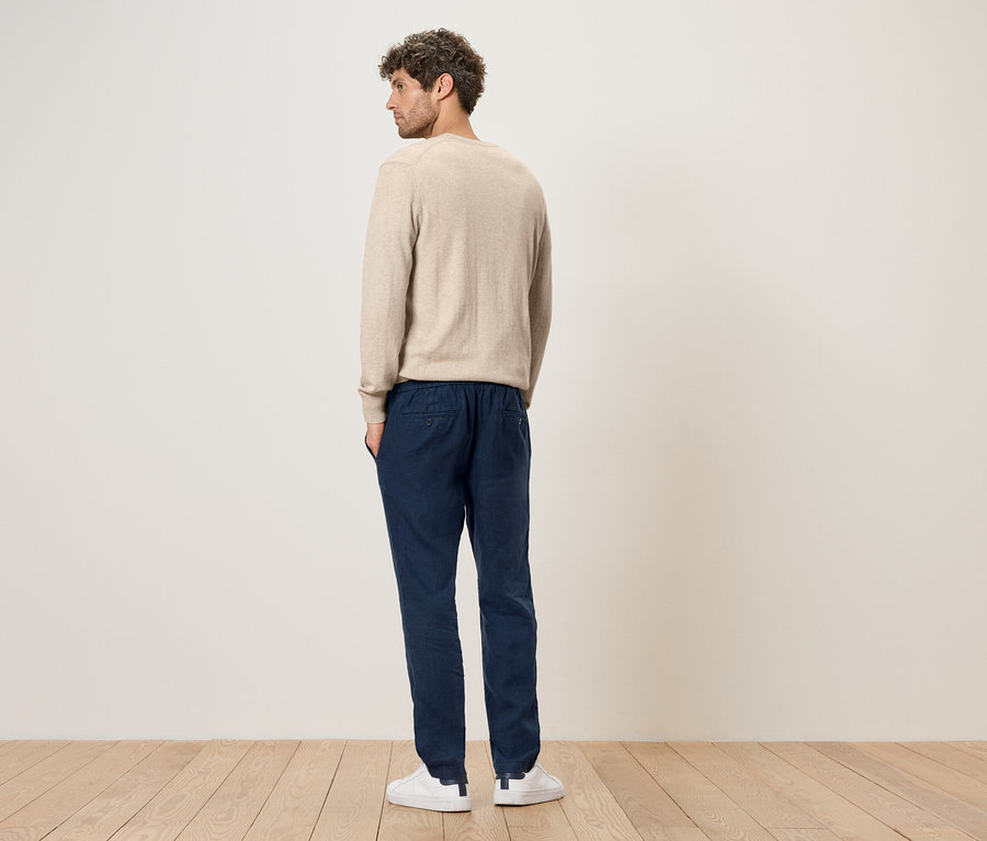 Mann von hinten in beigem Pullover, blauen Hosen und weißen Turnschuhen.