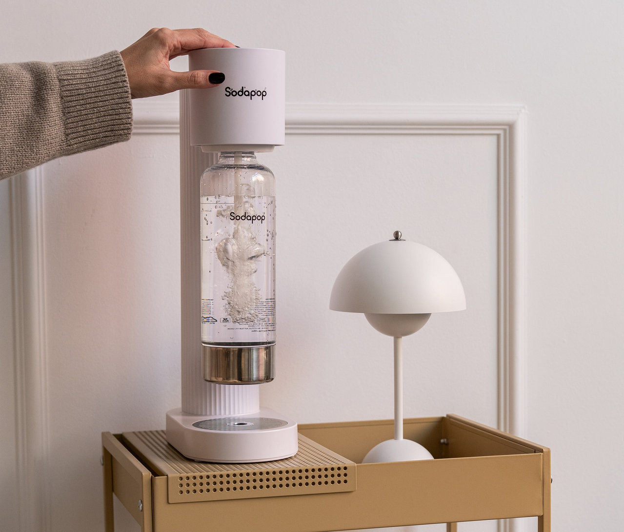 Hand betätigt weißen Sodapop Wassersprudler Cooper Pro inklusive 5 Flaschen auf einem Tisch.