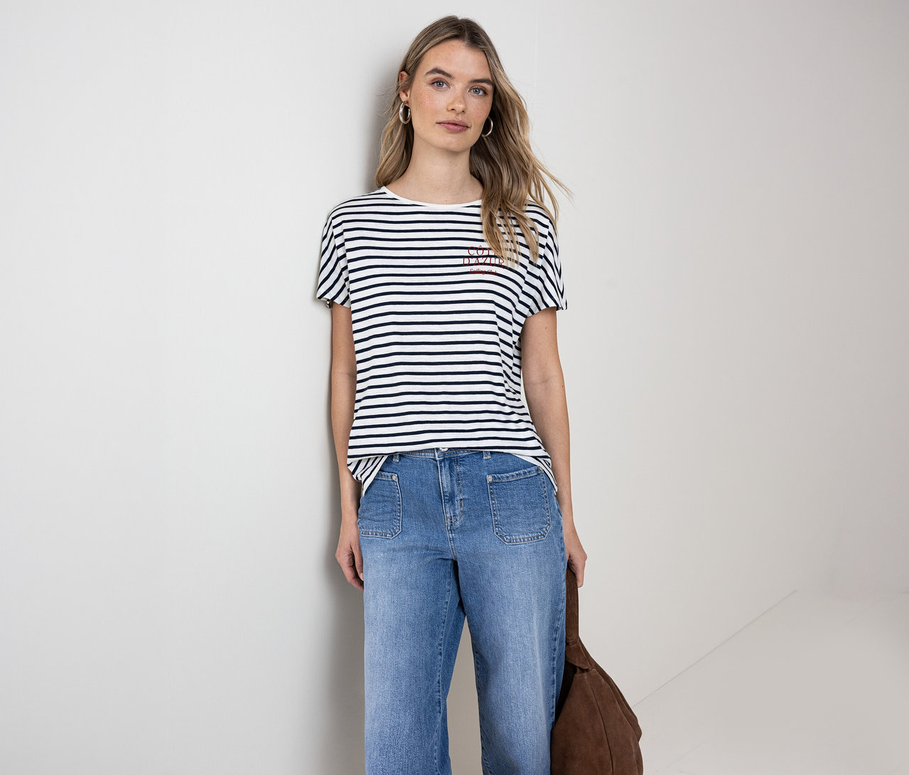 Frau trägt ein navy-weißes Street One T-Shirt, blaue Jeans und hält eine braune Tasche.