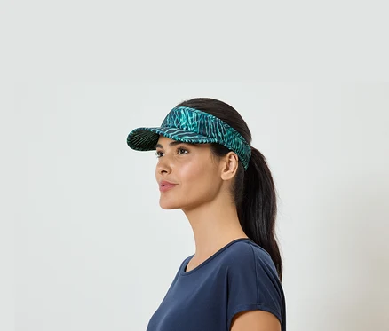 Frau mit Pferdeschwanz und blauem T-Shirt, trägt ein grünes Visor mit Blattmuster.