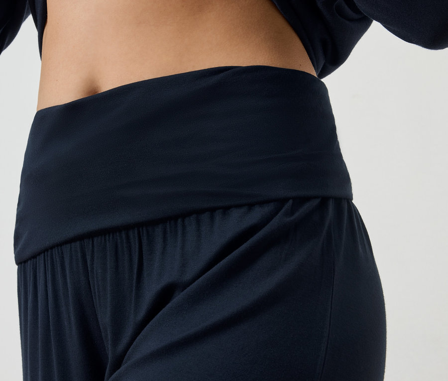 Nahaufnahme einer Frau, die marineblaue Yoga-Kleidung trägt, bestehend aus Hose und langärmligem Oberteil.