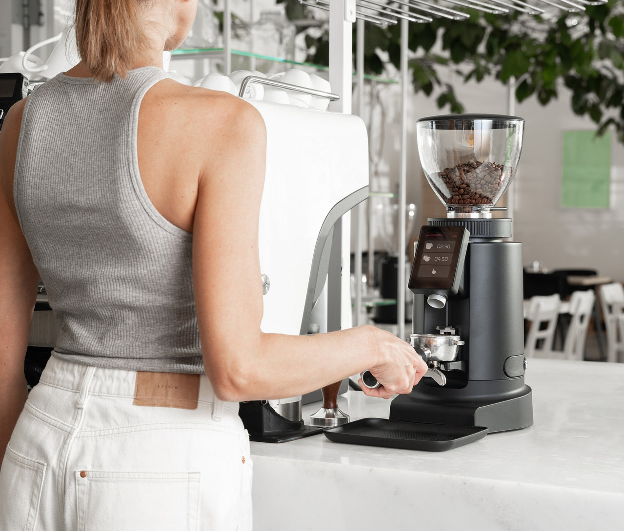 Frau befüllt Siebträger mit Kaffeemehl an einer Kaffeemühle.