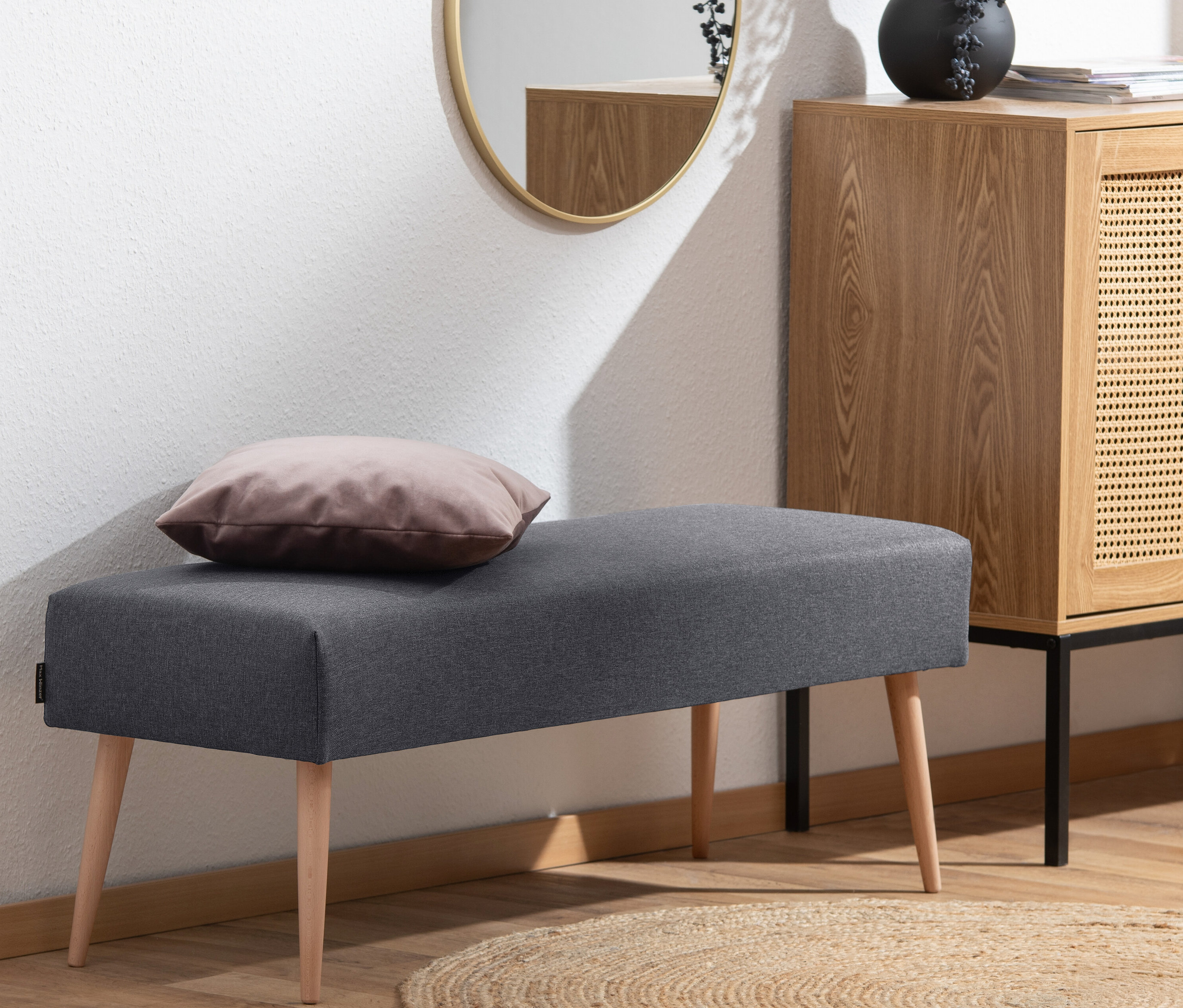 Eine graphitfarbene Sitzbank »Sit« mit einem Kissen darauf steht auf einem Teppich.