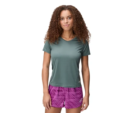 Frau mit lockigem Haar trägt ein grünes FILA Damen-Funktionsshirt und lila gemusterte Shorts.