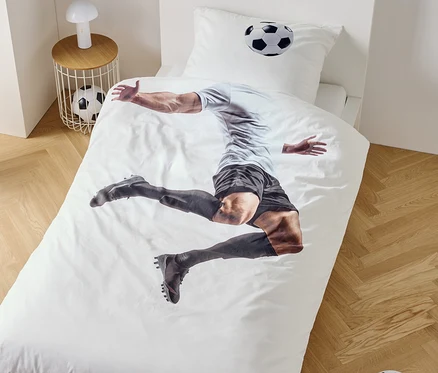 Auf einem Bettbezug ist ein Fußballspieler im Sprung abgebildet, daneben ein Nachttisch mit Lampe und Fußball.
