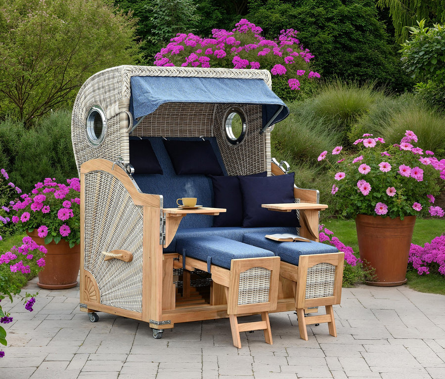 Ein geflochtener Strandkorb mit blauem Stoffdach und blauen Kissen steht auf einer Terrasse, umgeben von rosa blühenden Pflanzen.