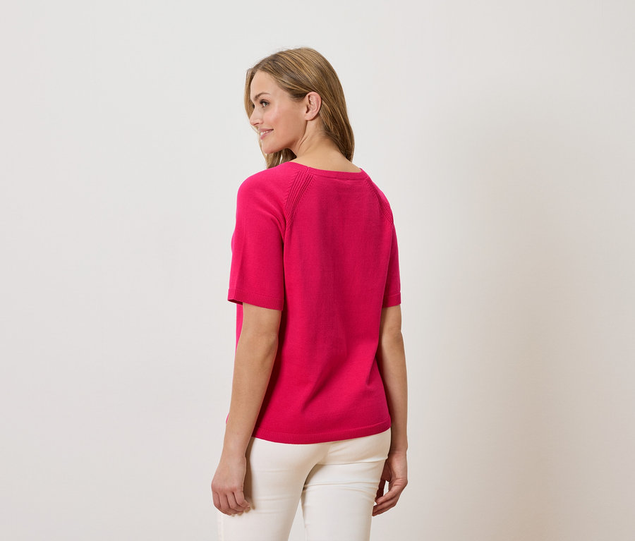 Frau trägt pinkes T-Shirt und weiße Hose, von hinten gesehen.