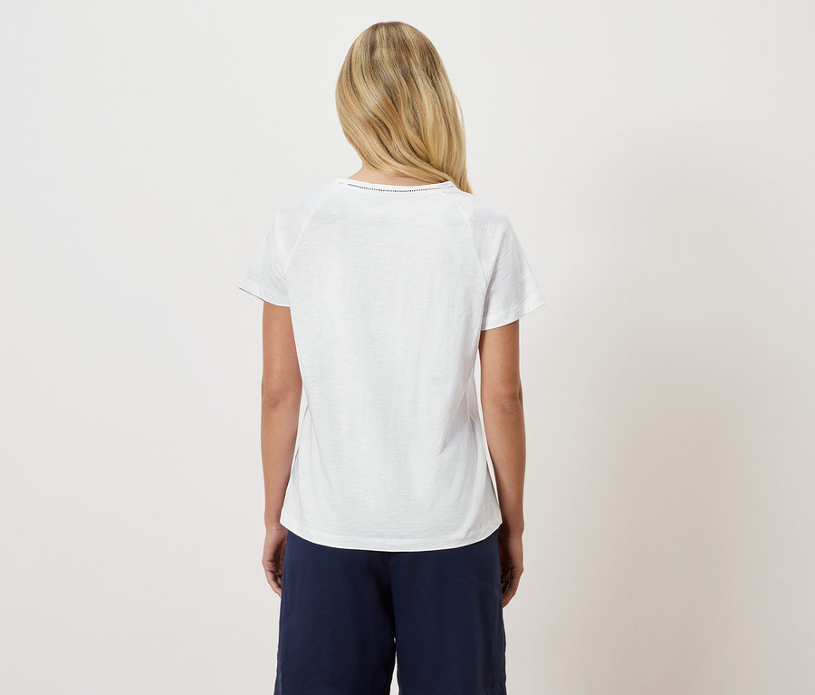 Rückansicht einer Frau mit blonden Haaren, die ein weißes T-Shirt und eine dunkelblaue Hose trägt.