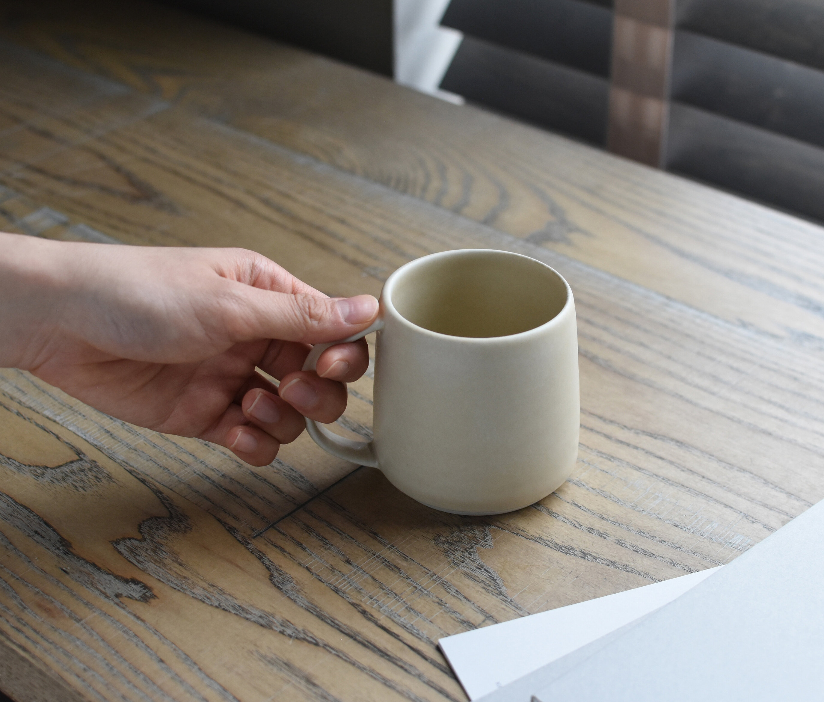 Hand hält eine cremefarbene Tasse auf einem Holztisch.