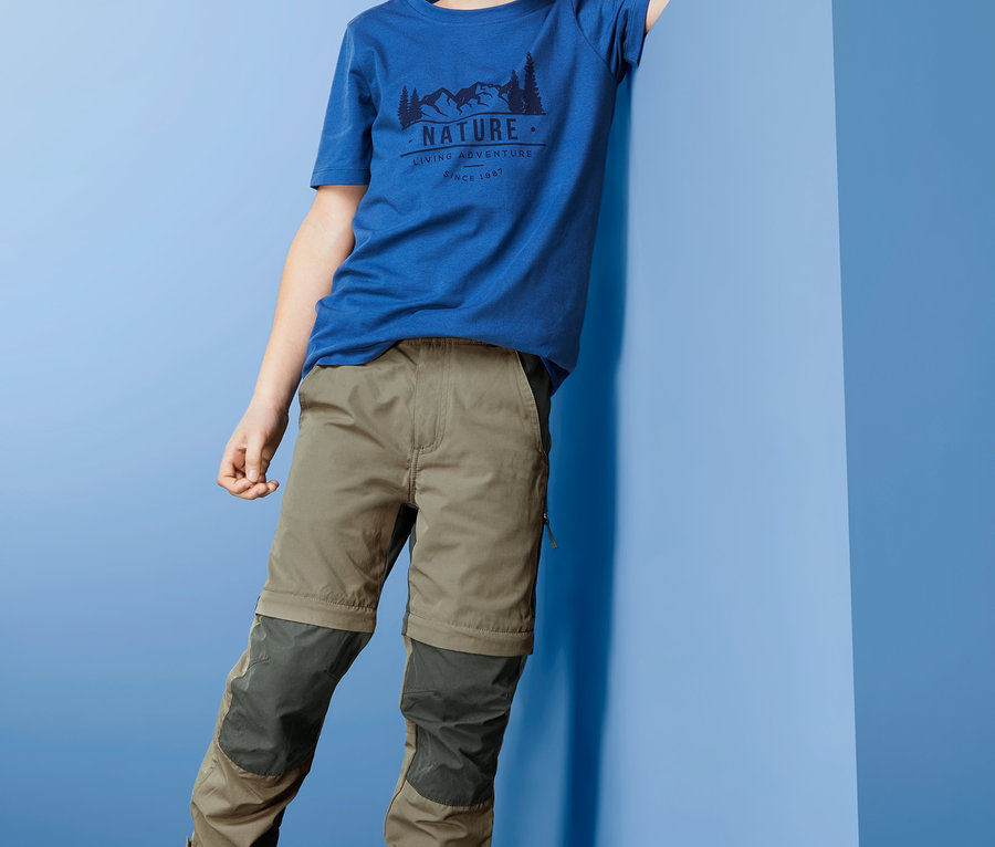 Junge posiert in blauem T-Shirt und 2-in-1-Funktionshose.