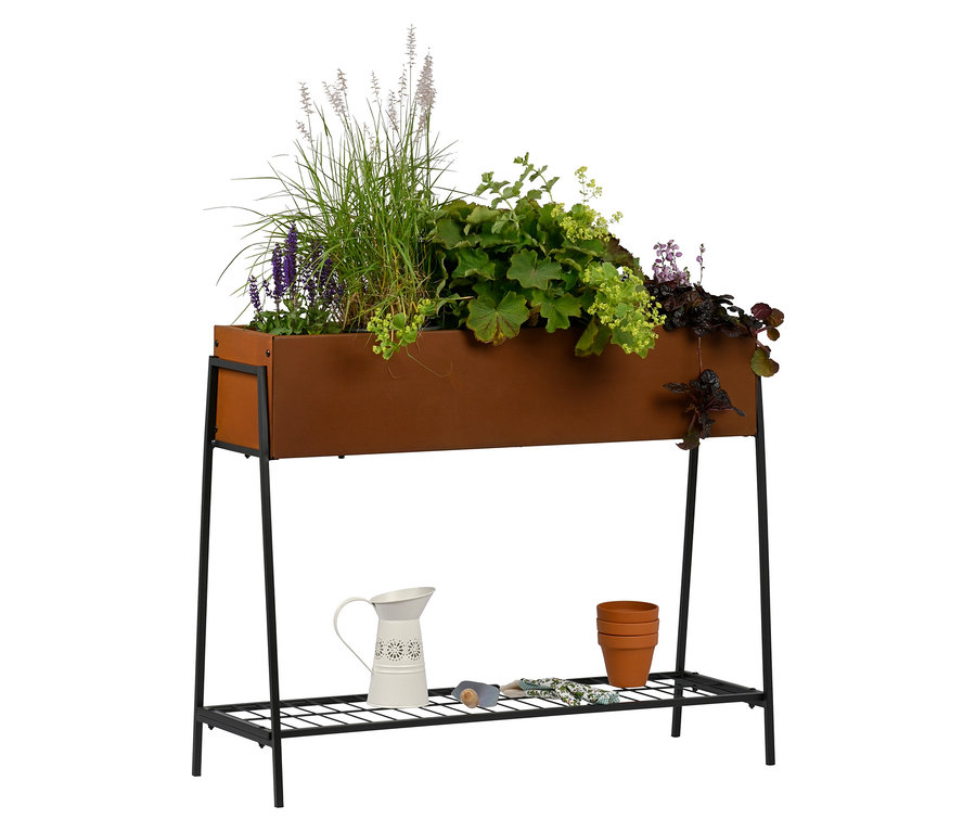 Verschiedene Pflanzen in einem Hochbeet mit Ablage in Edelrost-Optik, stehend auf einem schwarzen Metallgestell. Auf der Ablage stehen eine weiße Kanne und drei übereinander gestapelte Tontöpfe.