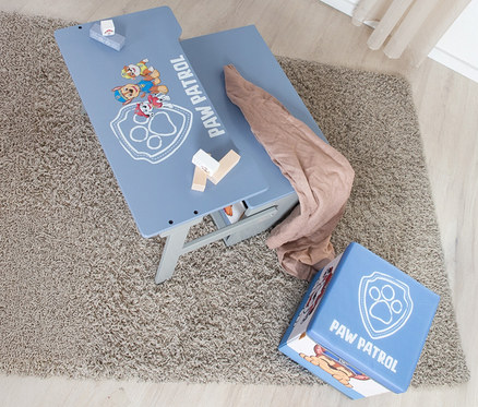 Draufsicht auf einen Paw Patrol Kindertisch mit Spielzeug und einem Paw Patrol Hocker auf einem Teppich.