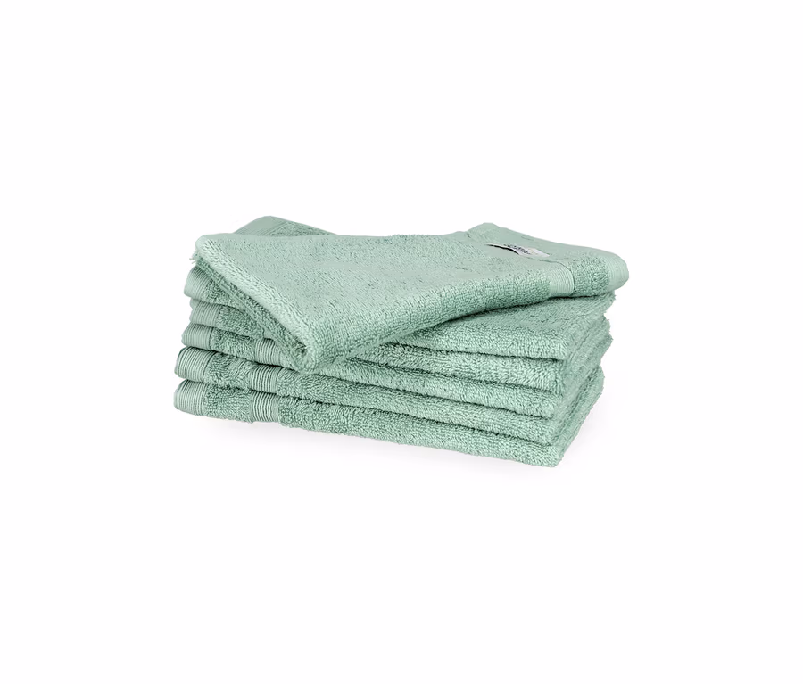 Stapel von sechs salbeigrünen SCHÖNER WOHNEN-Kollektion Cuddly Gästehandtüchern auf weißem Hintergrund. Das oberste Handtuch liegt leicht schräg.
