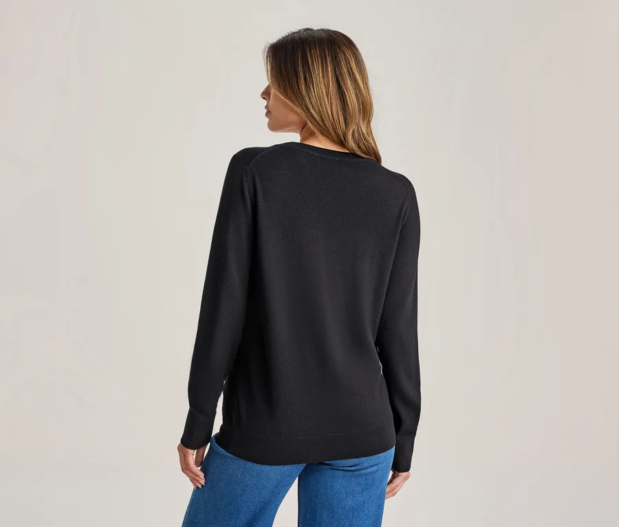 Frau von hinten, trägt einen schwarzen Langarmpullover und blaue Jeans, der Kopf leicht nach rechts gedreht.