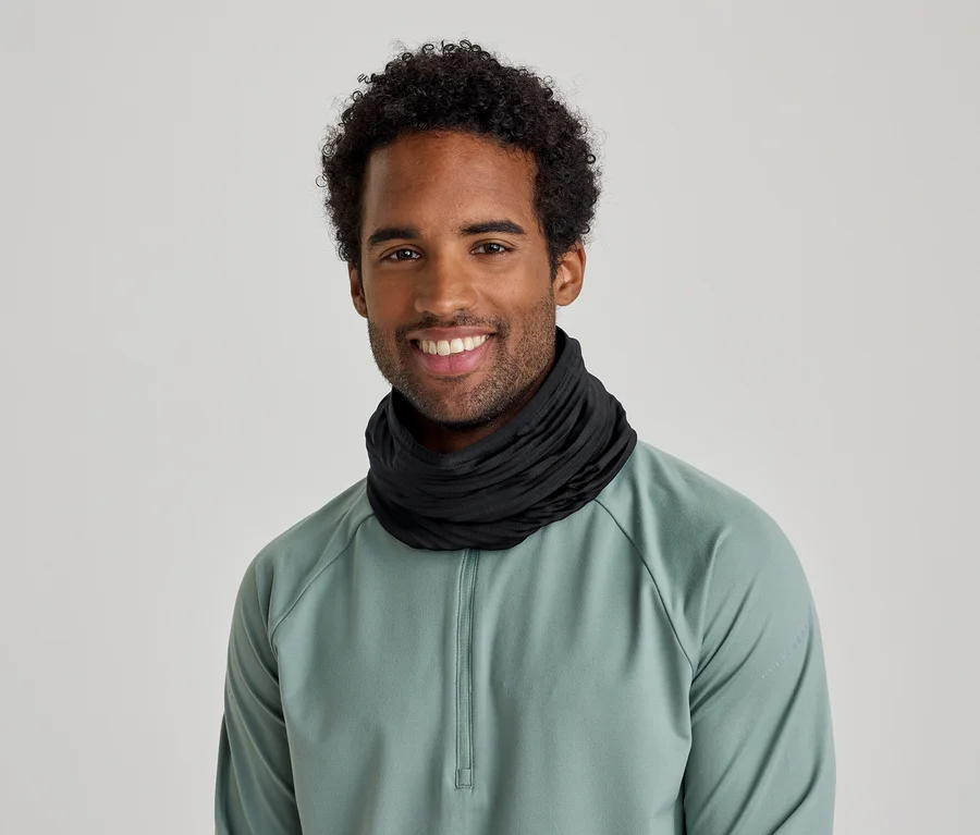 Ein lächelnder Mann mit lockigem Haar trägt einen schwarzen Halswärmer und ein hellgrünes Langarmshirt.