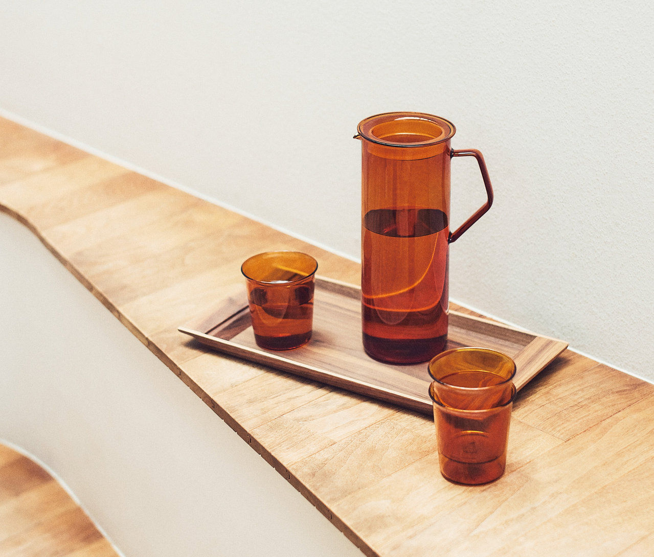 KINTO Krug »Cast Amber« mit Wasser und zwei passenden Gläsern auf einem Holztablett auf einer Holzoberfläche.