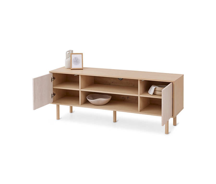 Helles Holz-Sideboard mit offenen Fächern und zwei leicht geöffneten Türen. Oben stehen eine weiße Vase und ein gerahmtes Bild. In den Fächern sind eine Holzschale und weiße Teller mit einem Tuch.